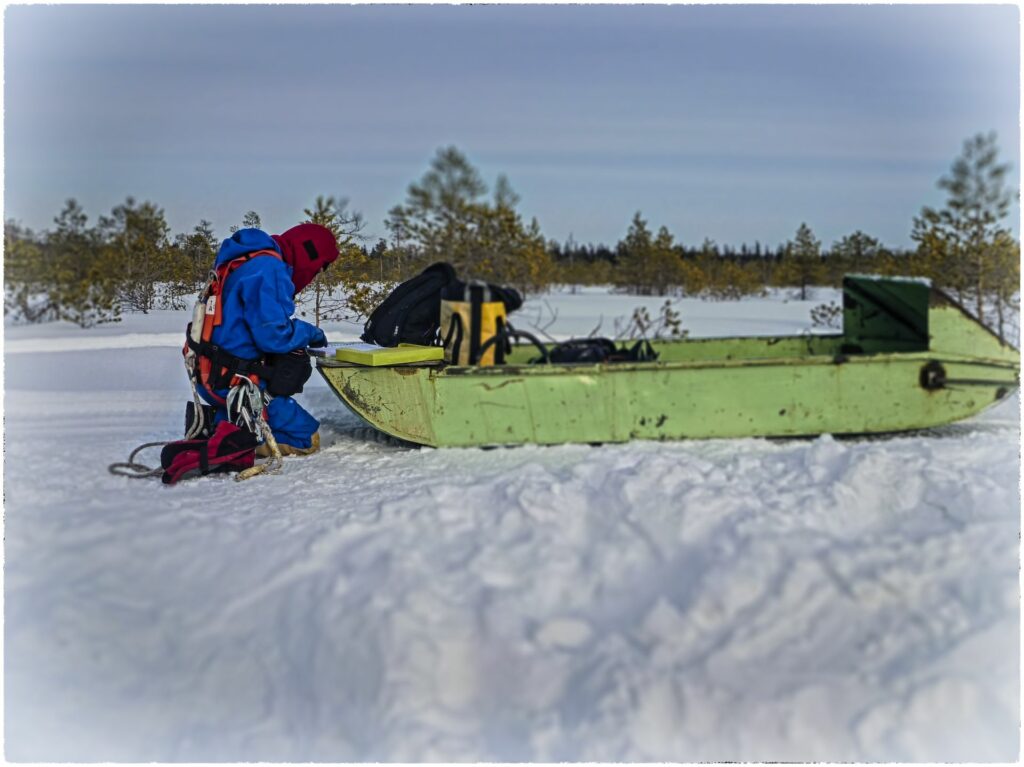 working person kneeling in snownext ti a gree snowmobile trailer