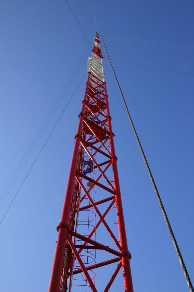 person climbing the red and white tall tower in Zotto with clear blue sky