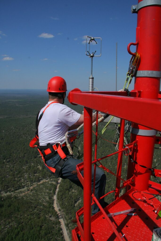 Mechanic in climbing equipment outside working high up on the tower